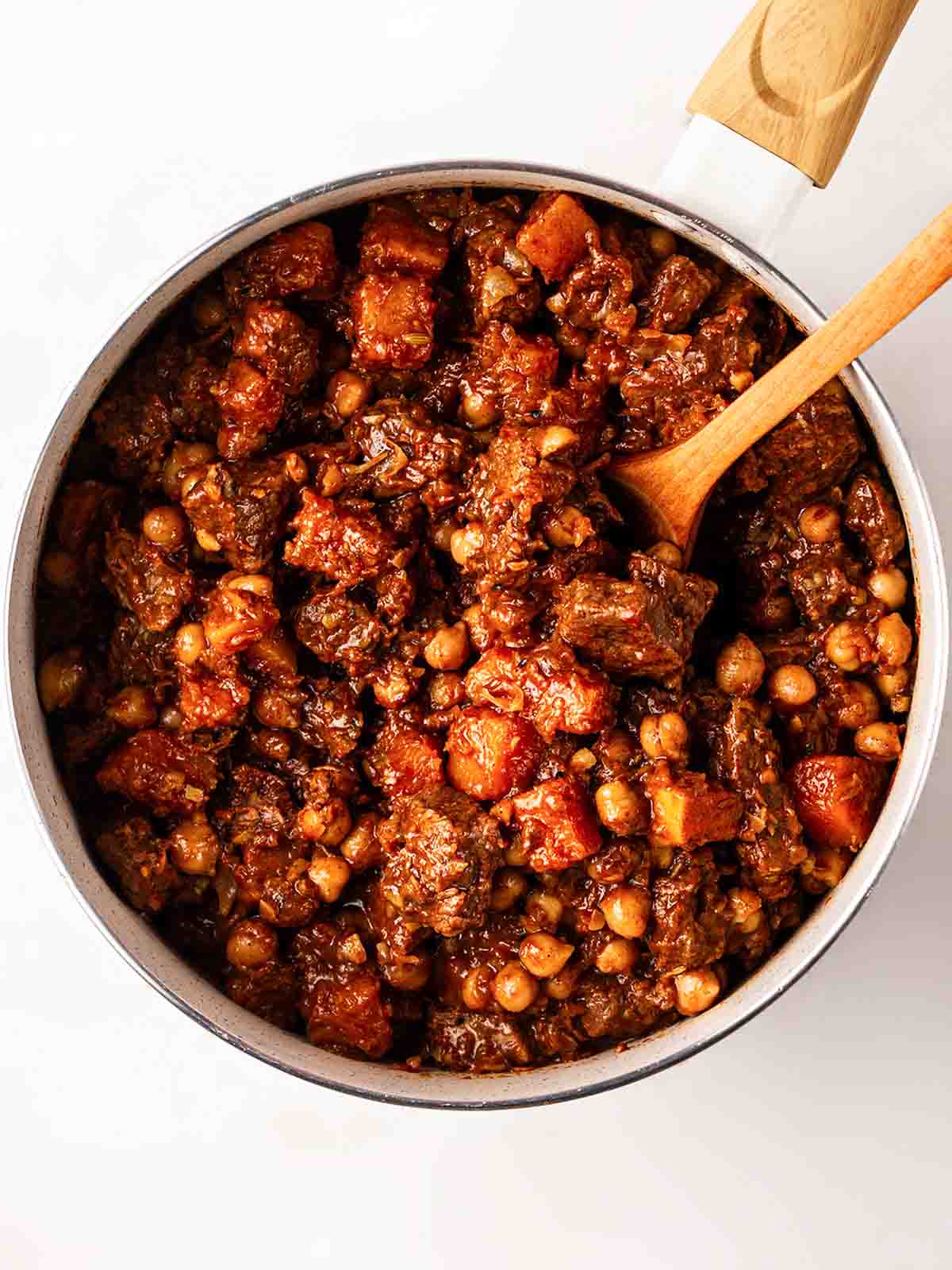 A large pan filled with Lamb Tagine with a wooden spoon sticking out, ready to serve.