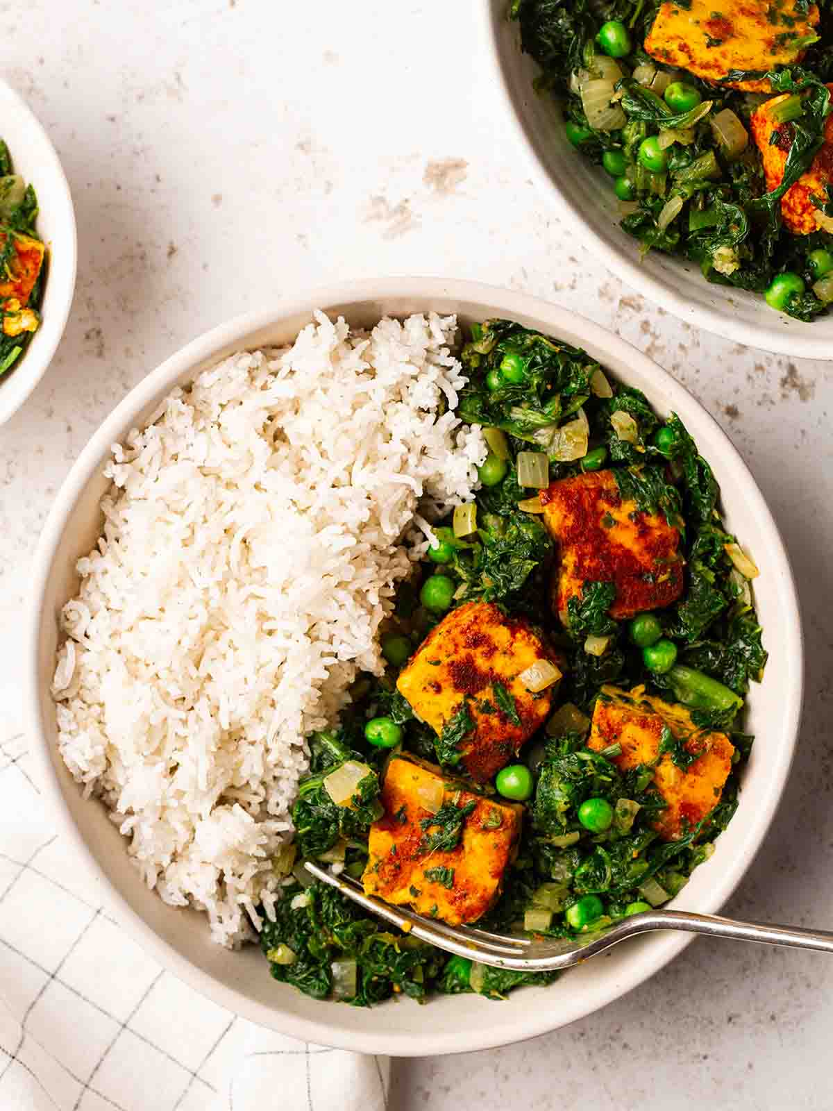 Two bowls of palak paneer and rice with forks on a table, ready to eat.