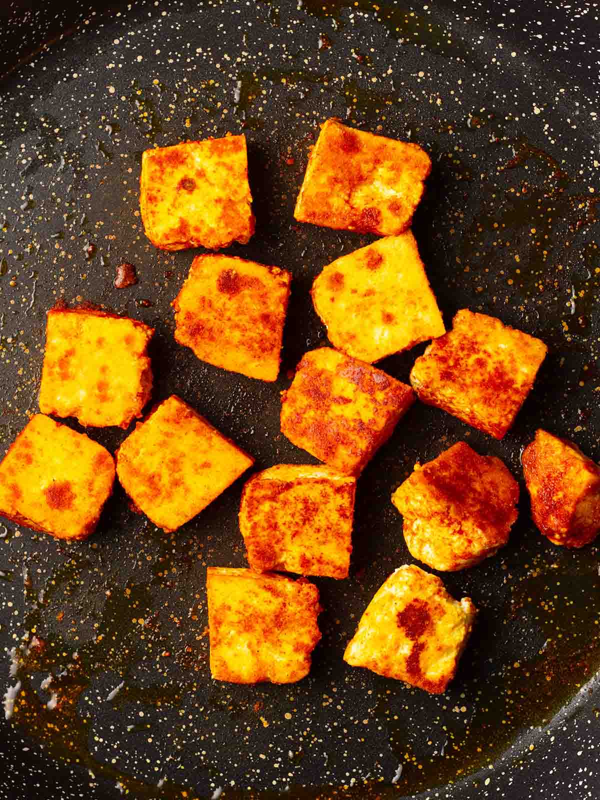 A close up of a frying pan with paneer being cooked, for step 1 in the process of cooking palak paneer.