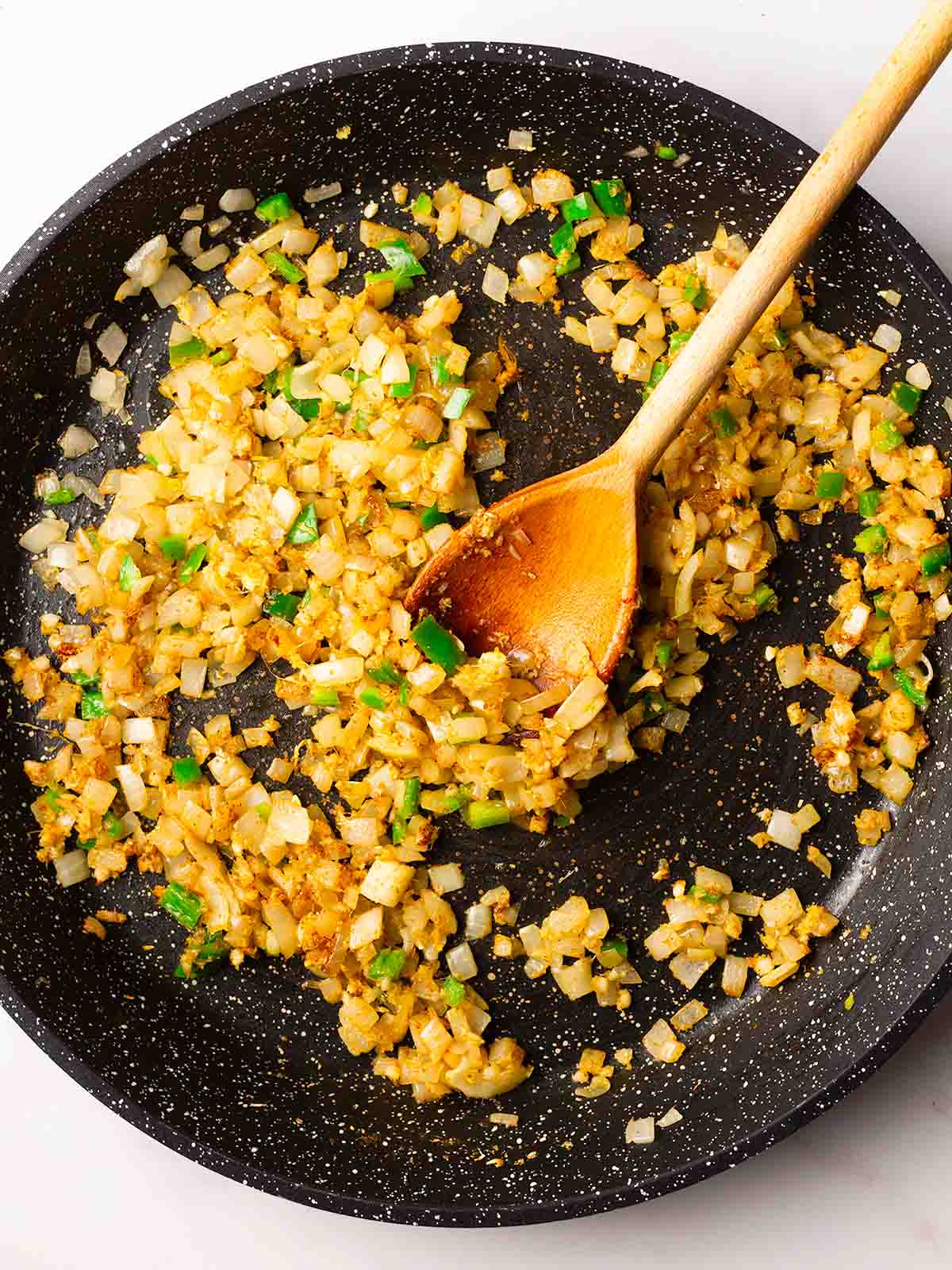 Onions and chilli frying in a pan with a wooden spoon in for step 2 in the recipe for Palak Paneer.