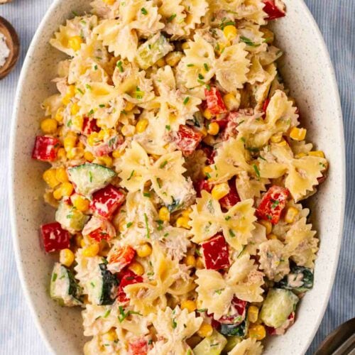 Sweetcorn, tuna, pasta, cucumber and peppers with dressing in a bowl.
