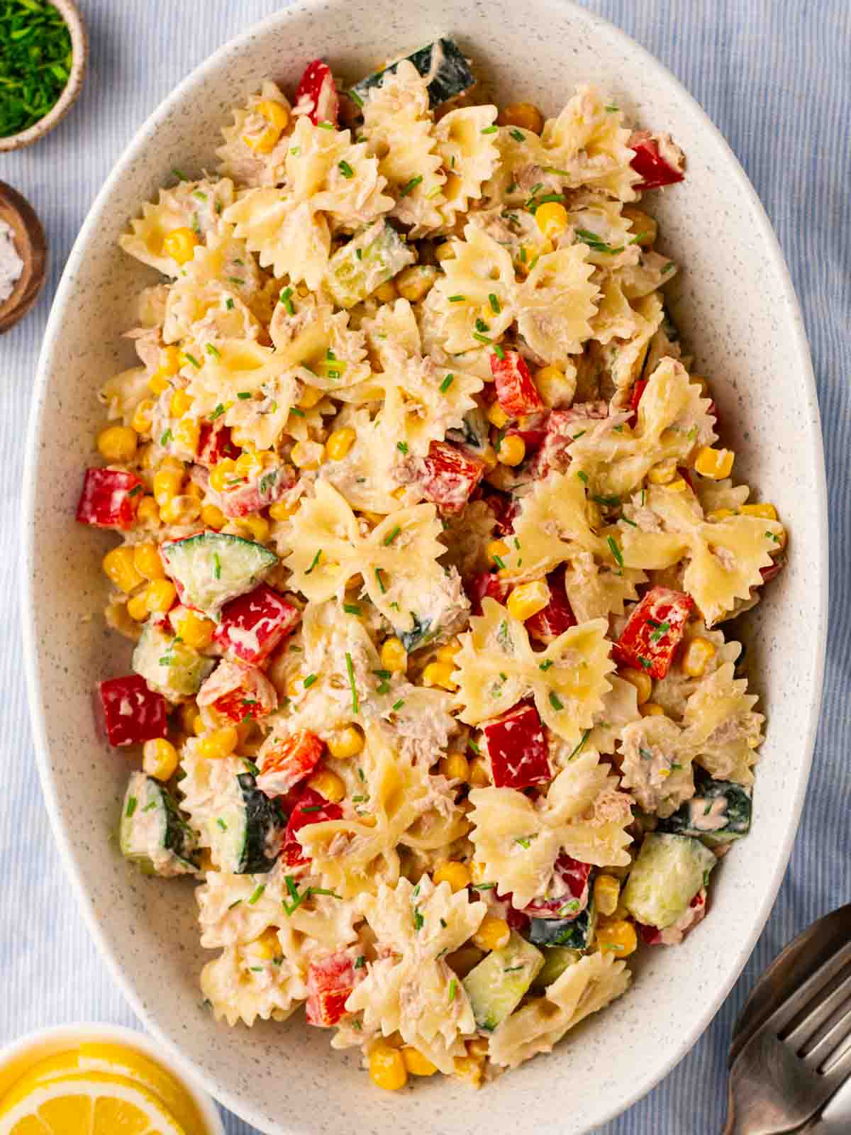 Sweetcorn, tuna, pasta, cucumber and peppers with dressing in a bowl.