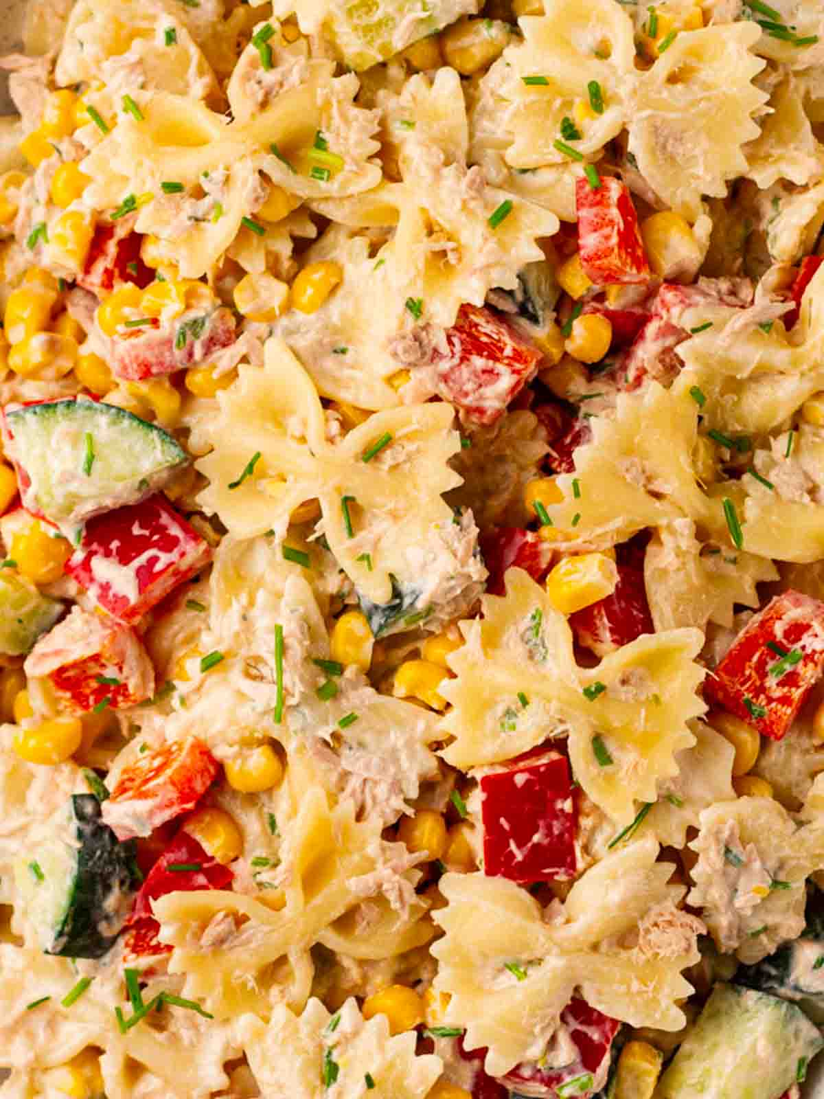 A close up of sweetcorn, tuna, pasta, cucumber and peppers with dressing in a bowl.