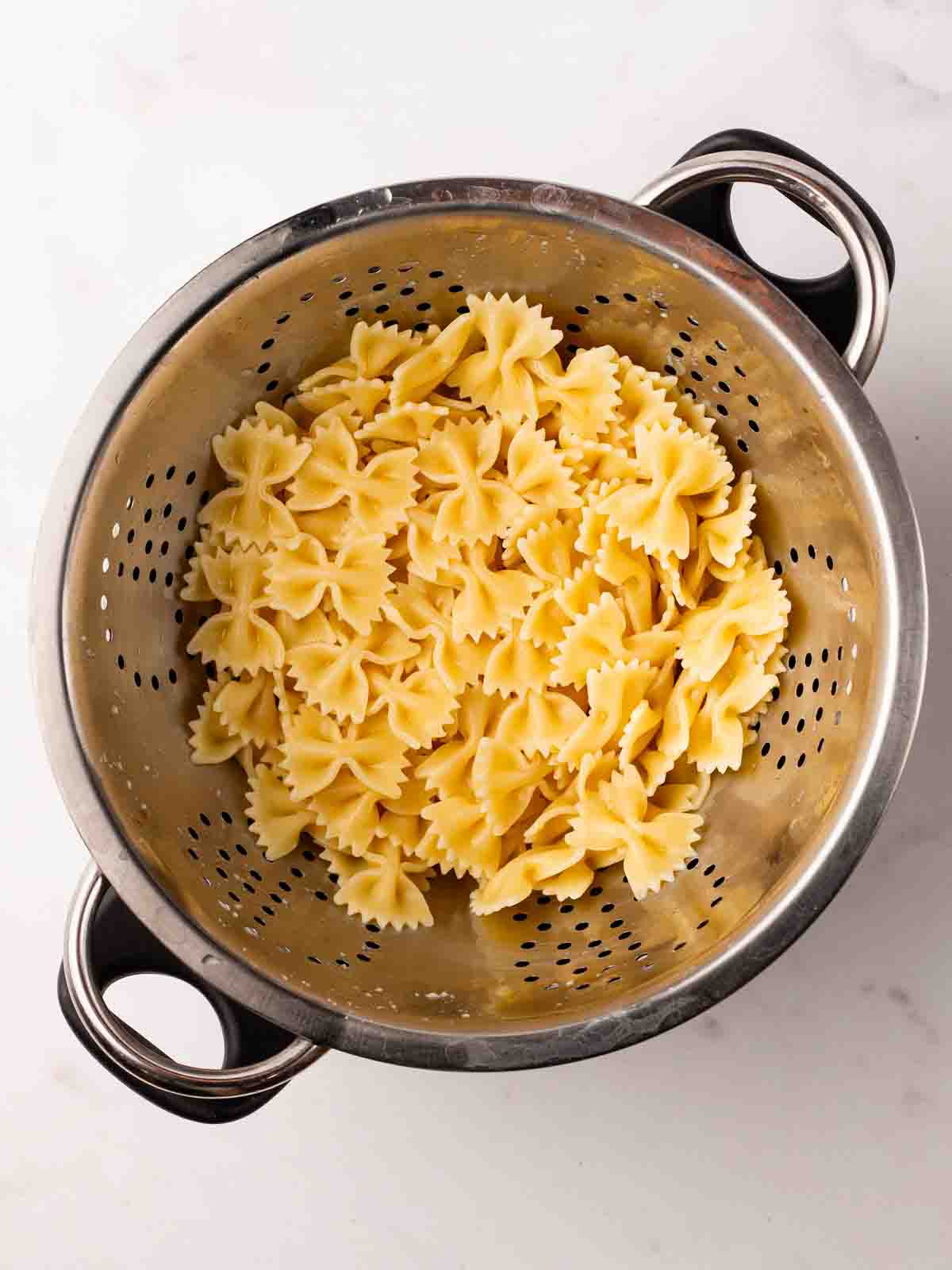 Cooked pasta bow ties in a colander for step 1 in the recipe for Tuna Pasta Salad.