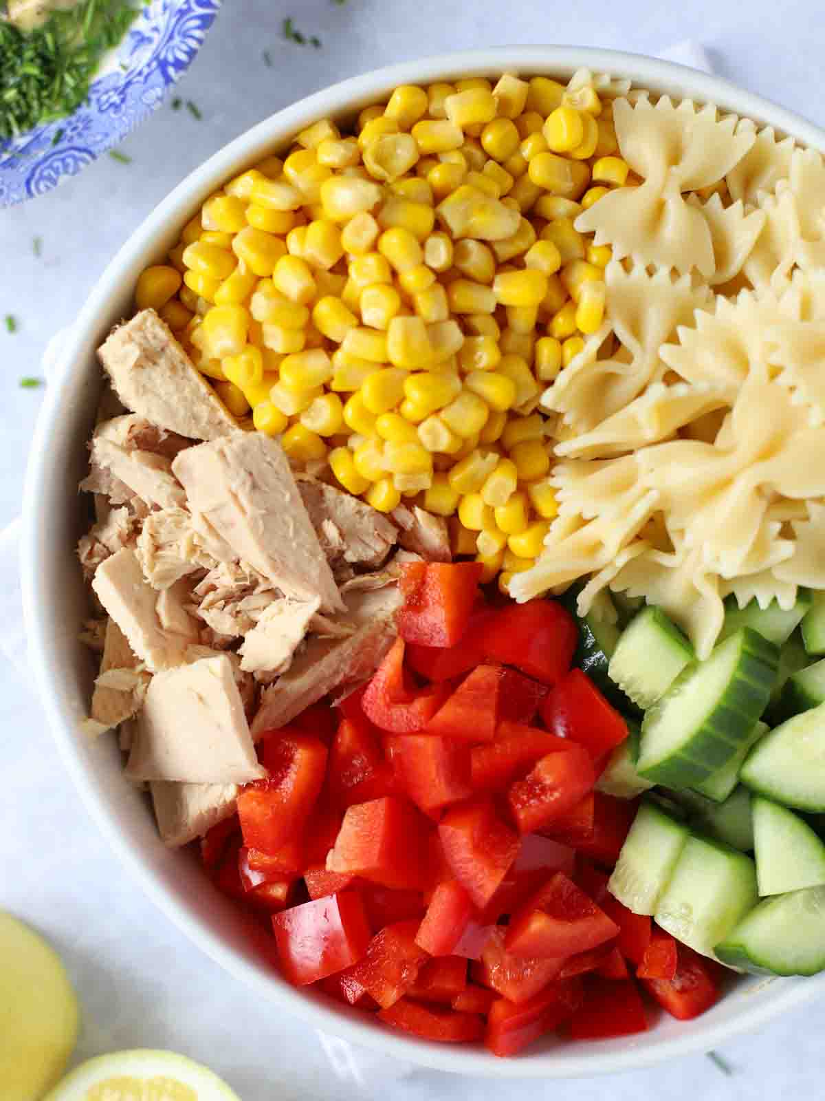 A bowl with ingredients for tuna pasta salad, ready to be mixed.