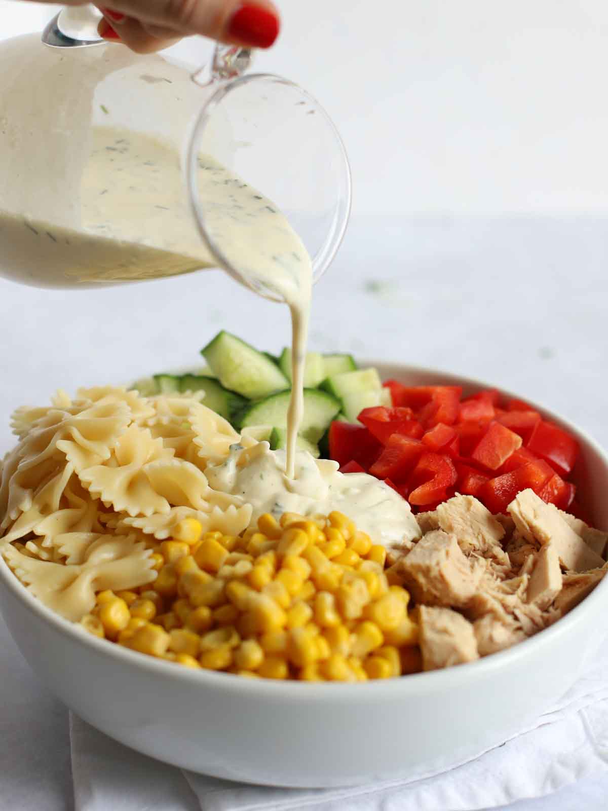 Tuna pasta and vegetables with salad dressing being poured on.