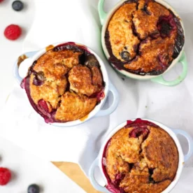 Three small ramekins filled with Baked Oats with blueberries and a golden top, on a white tablecloth.