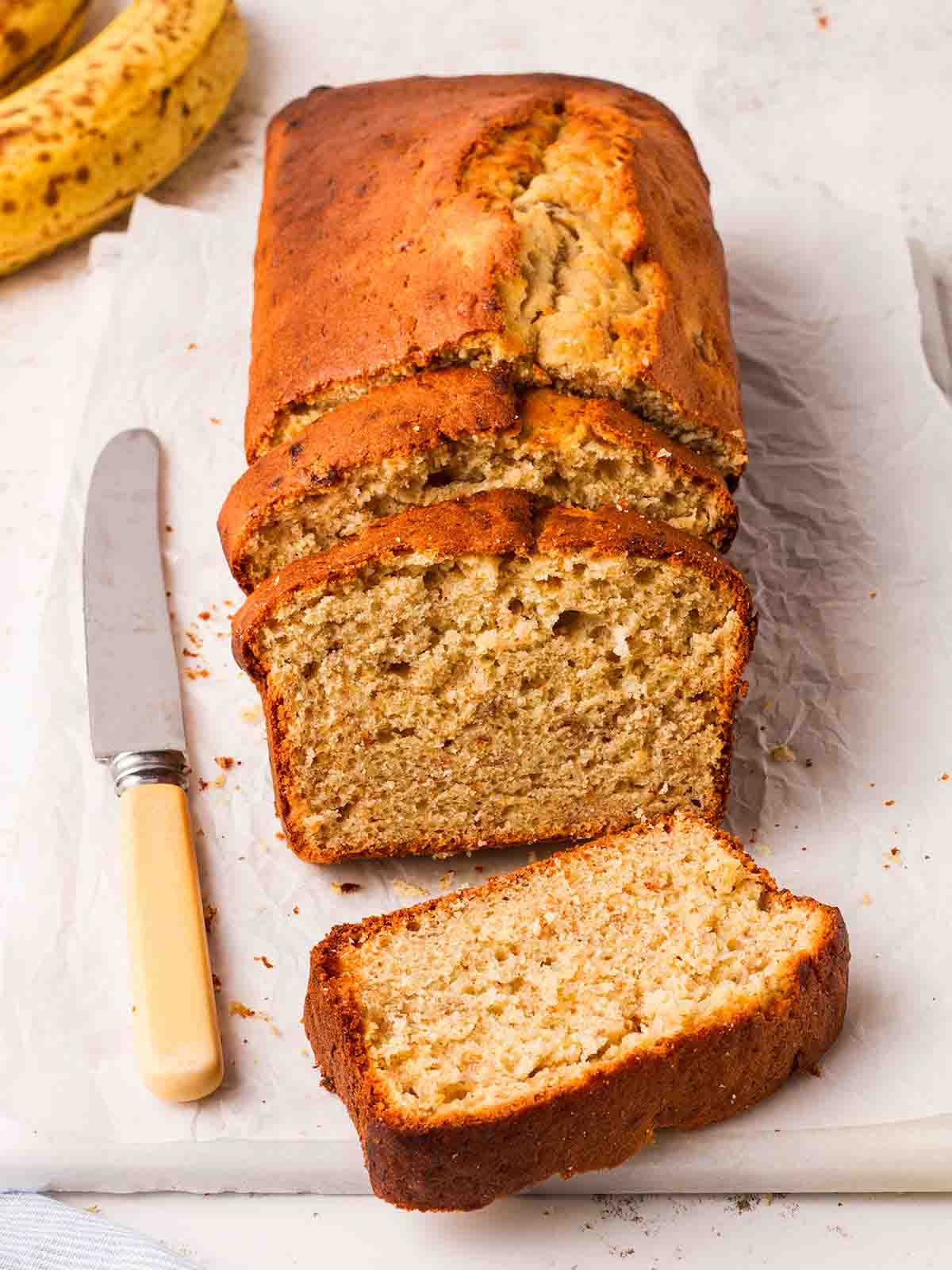 A side view of a half sliced banana loaf cake on a white board with a knife to the side.