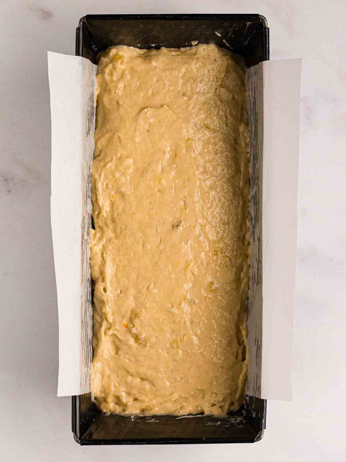 A loaf tin filled with raw cake mixture for step 3 in the recipe for Banana Cake.