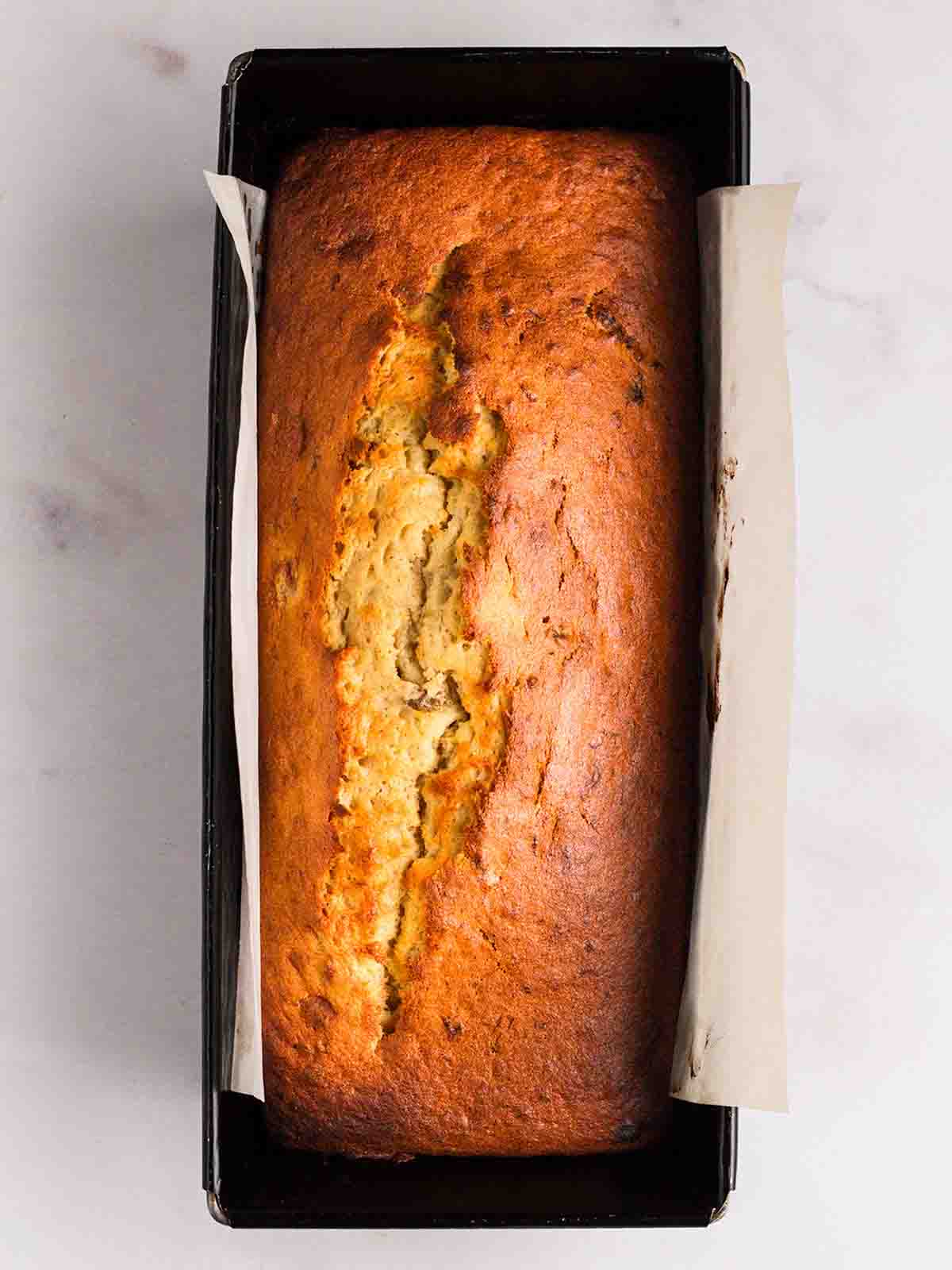 A bird's eye view of a baked banana cake in a loaf tin, straight out of the oven, for step 4 in the recipe for Banana Cake.