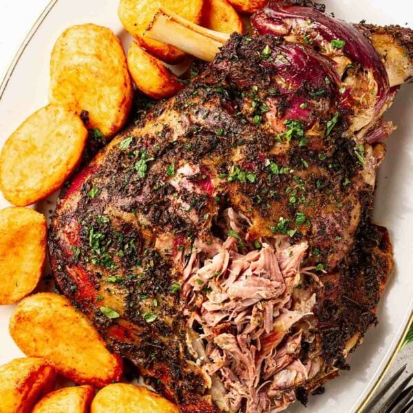 Roast lamb shoulder with a herb rub, next to roast potatoes.