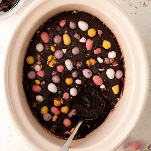 A slow cooker mini egg Easter pudding being served up with a spoon.