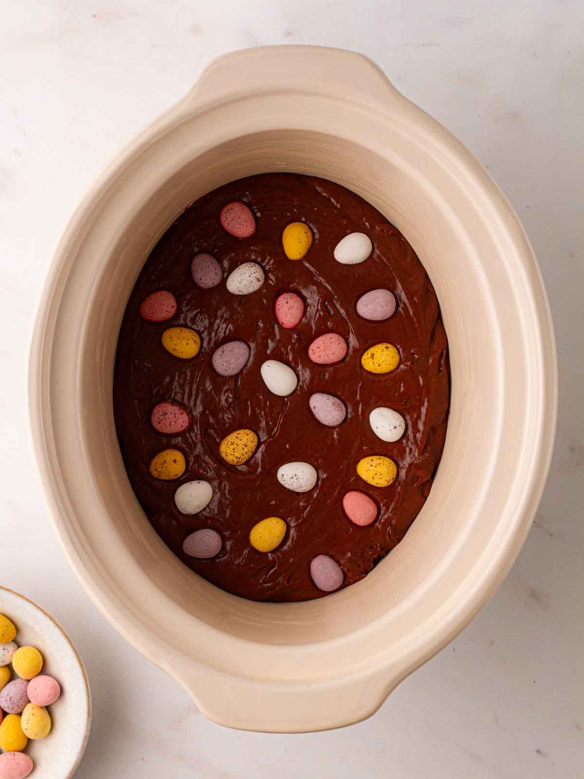 Chocolate mixture in a slow cooker pan with mini eggs on top for step 2 in the recipe for Slow Cooker Mini Egg Easter Pudding.