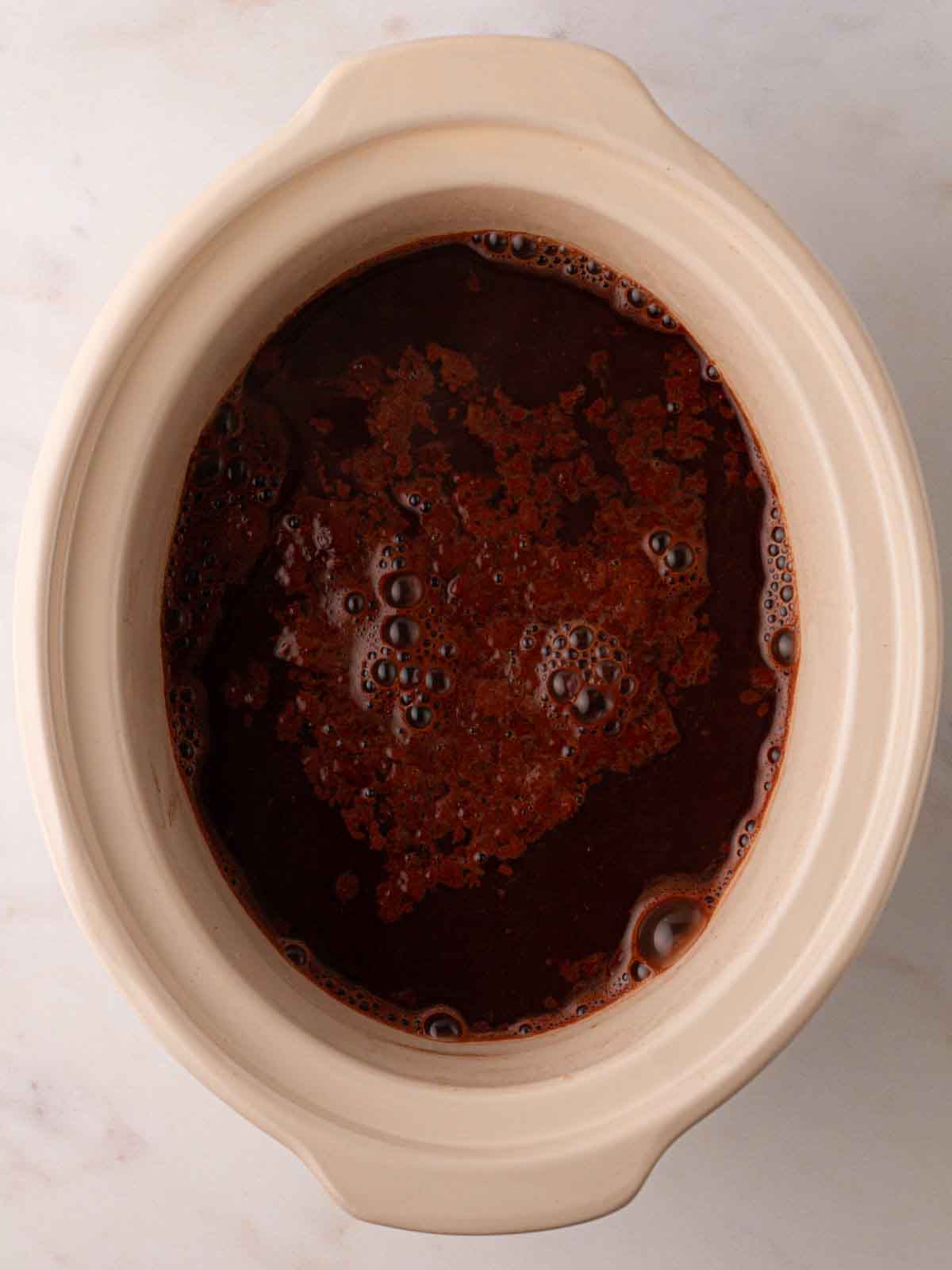 Chocolate mixture and water in a slow cooker pan for step 5 in the recipe for Slow Cooker Mini Egg Easter Pudding.