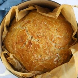 A crusty homebaked loaf cooked and ready to serve, in a pan with baking paper for the recipe No Knead Bread.