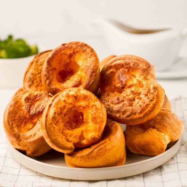 A pile of deliciously golden Yorkshire Puddings on a plate on a table, ready to serve.