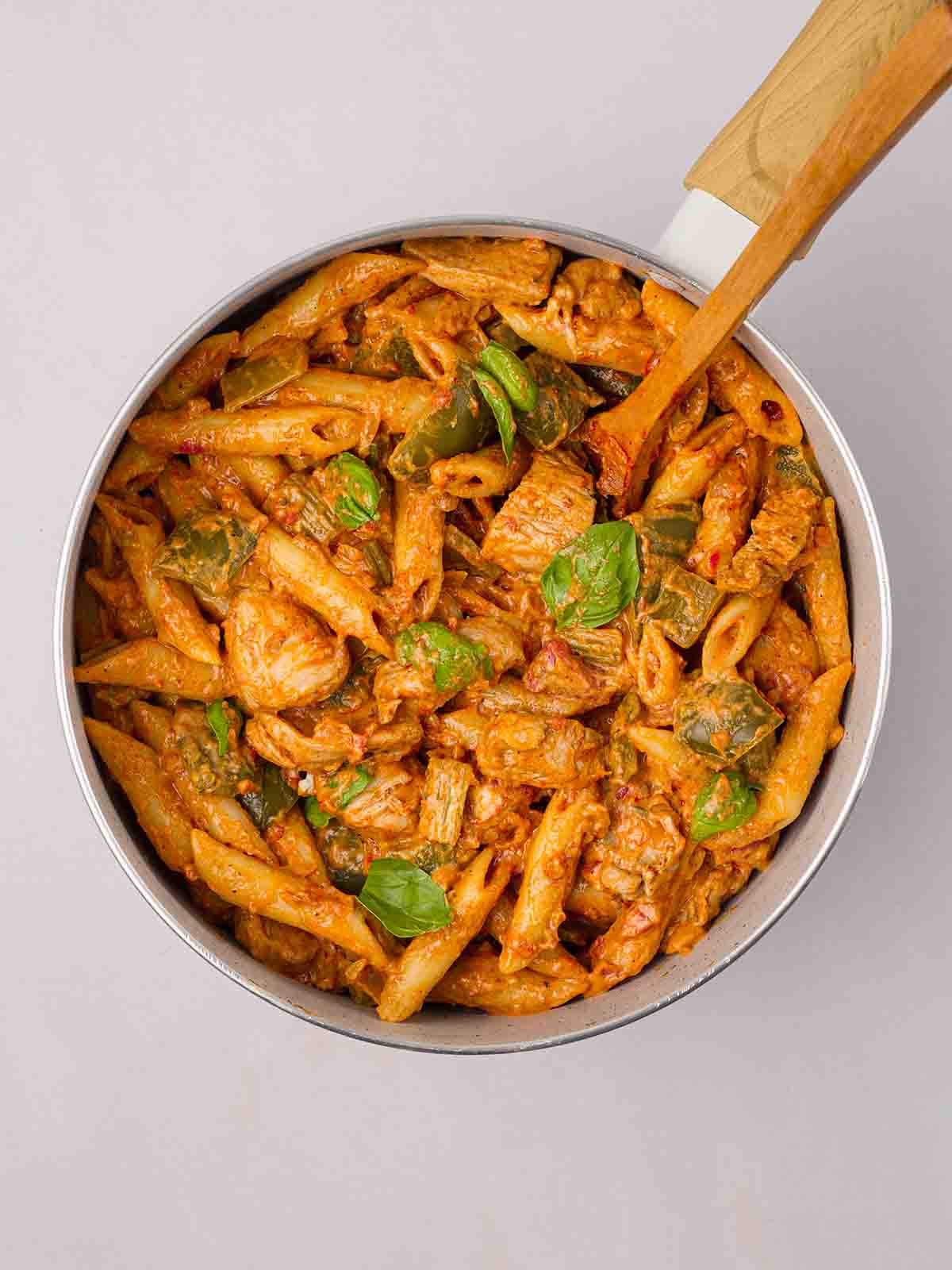 Cooked pasta in a pan with chicken, vegetables and basil on top with a cajun sauce for a one pot recipe.
