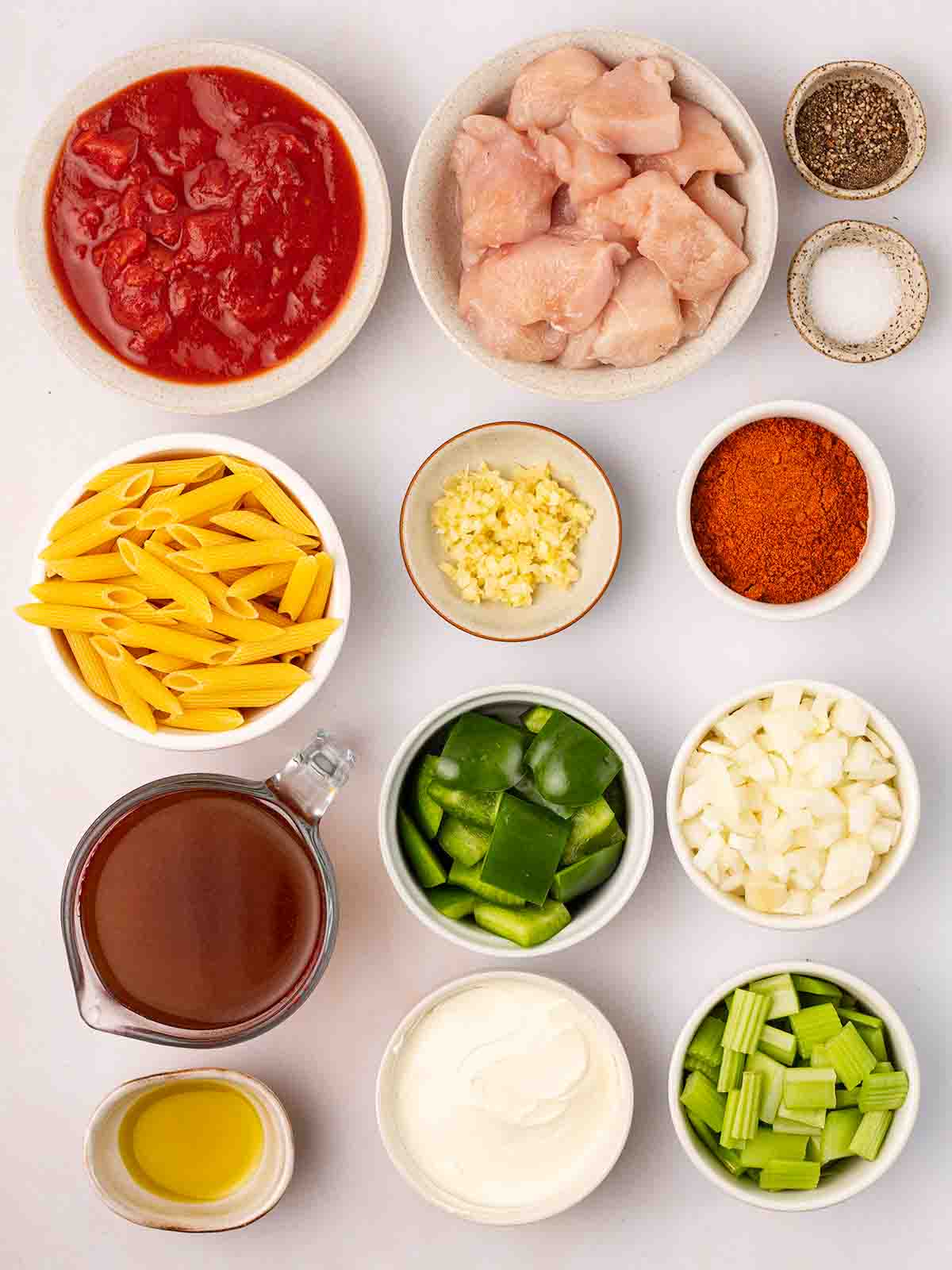 Ingredients for Cajun Chicken Pasta recipe in bowls laid out on a white counter top.