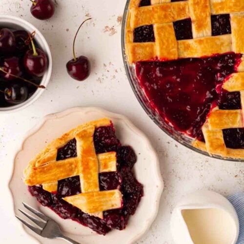 A cherry pie with a portion missing, and a slice on a plate with a fork, ready to eat.