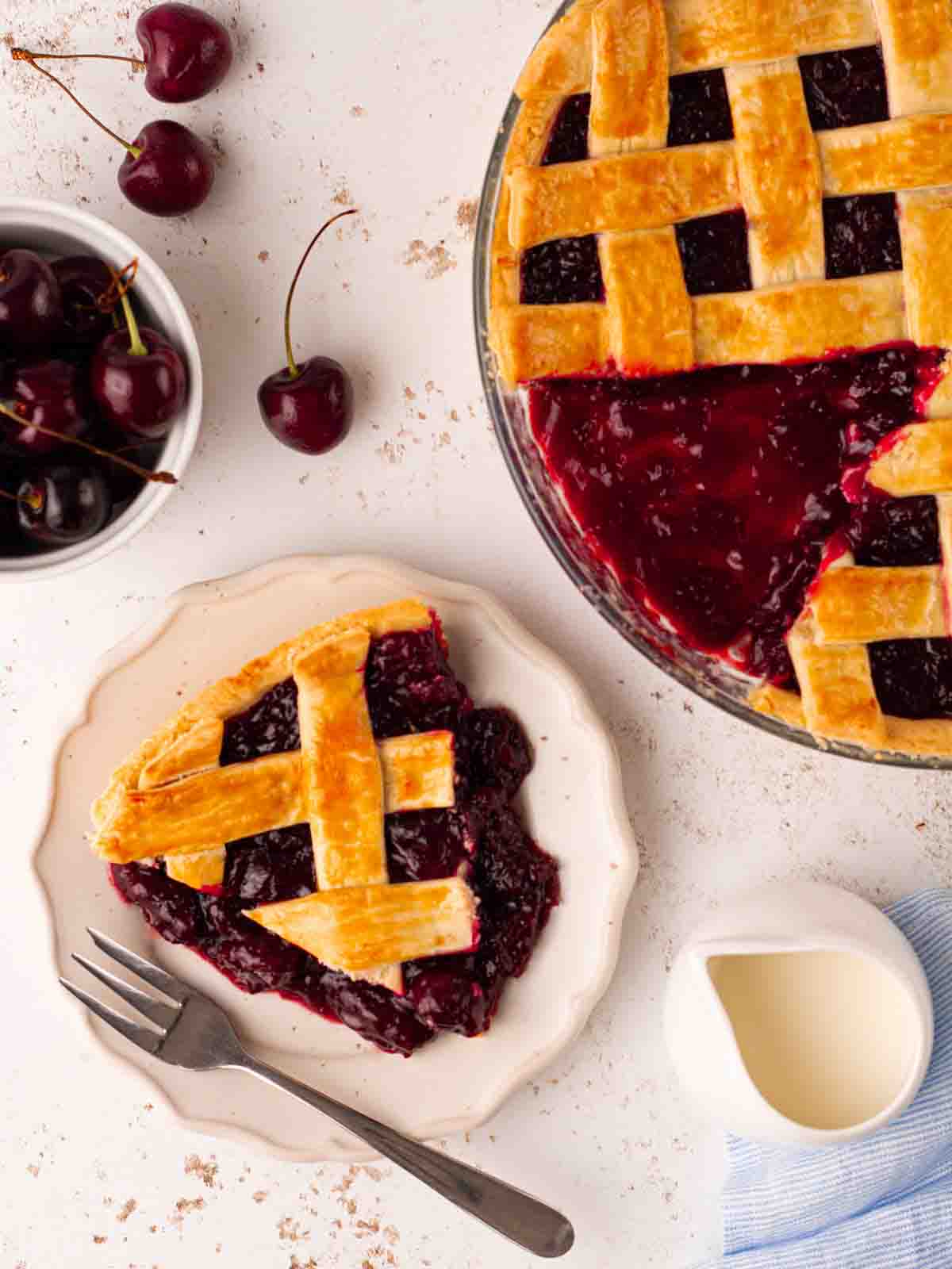 A homemade cherry pie with a lattice topping, with a portion on a plate, ready to eat.