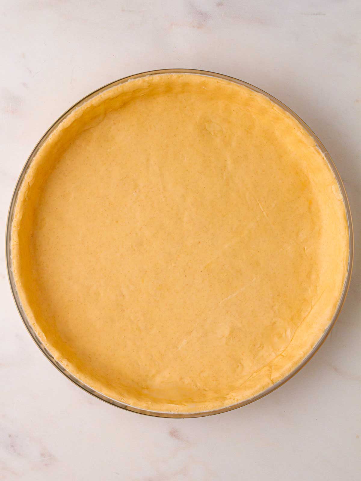 A plain pastry bottom in a round pie dish, ready to be filled with cherry pie filling.