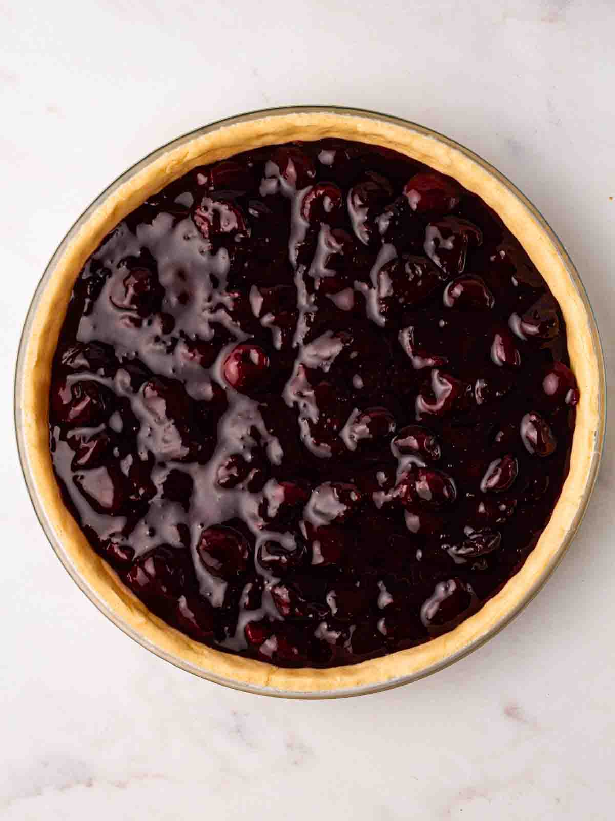 Cherry pie filling inside a tin with pastry, ready to have the topping put on.