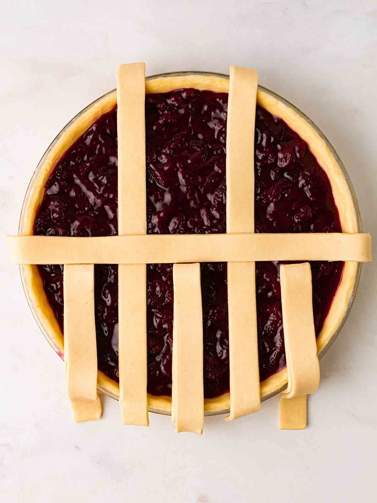 Looking down on an unbaked cherry pie, with a partially constructed lattice topping for step 5 in the recipe.