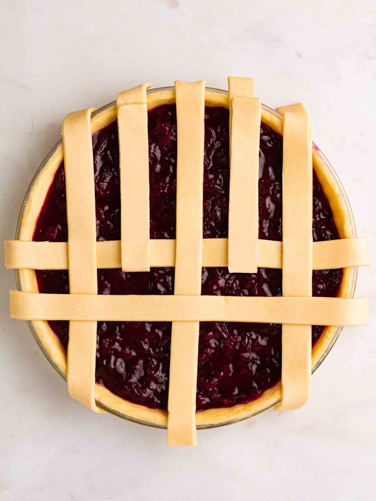 Looking down on an unbaked cherry pie, with a partially constructed lattice topping for step 6 in the recipe.