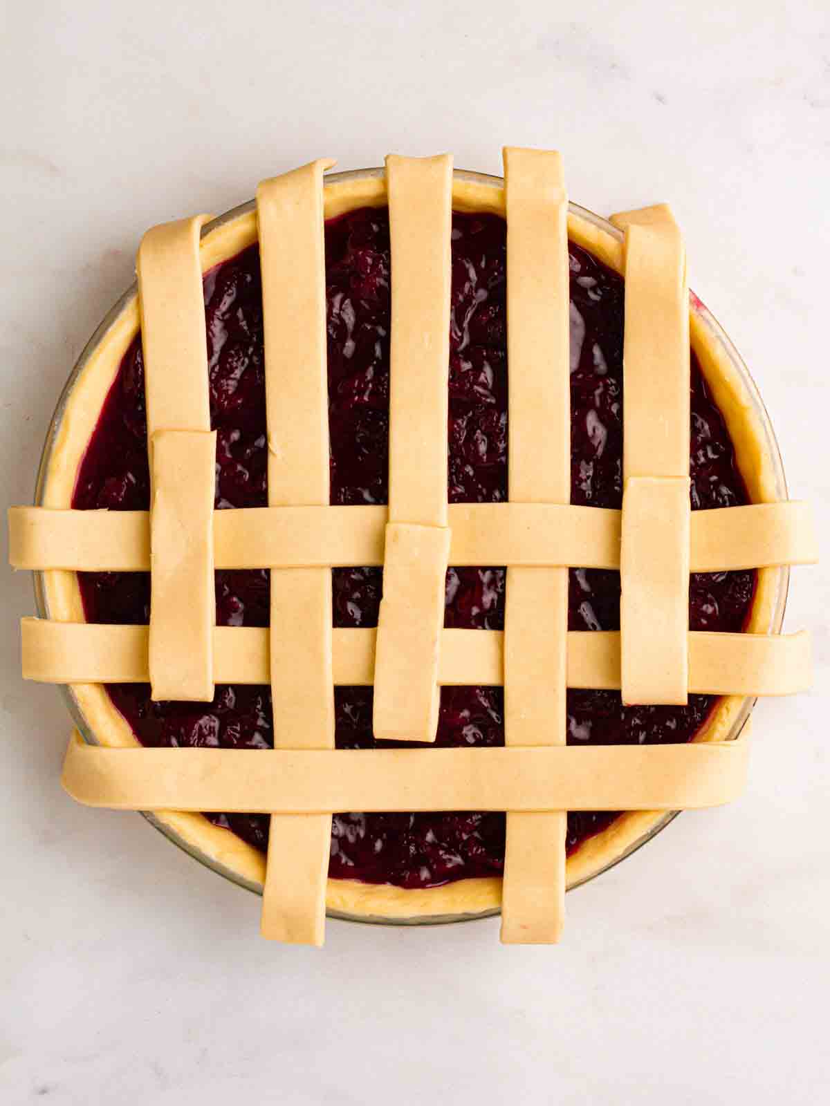 Looking down on an unbaked cherry pie, with a partially constructed lattice topping for step 7 in the recipe.