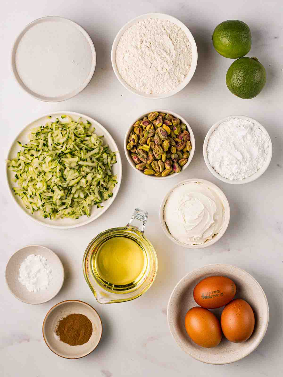 The ingredients for making a Courgette Cake, measured out in bowls on a white surface.