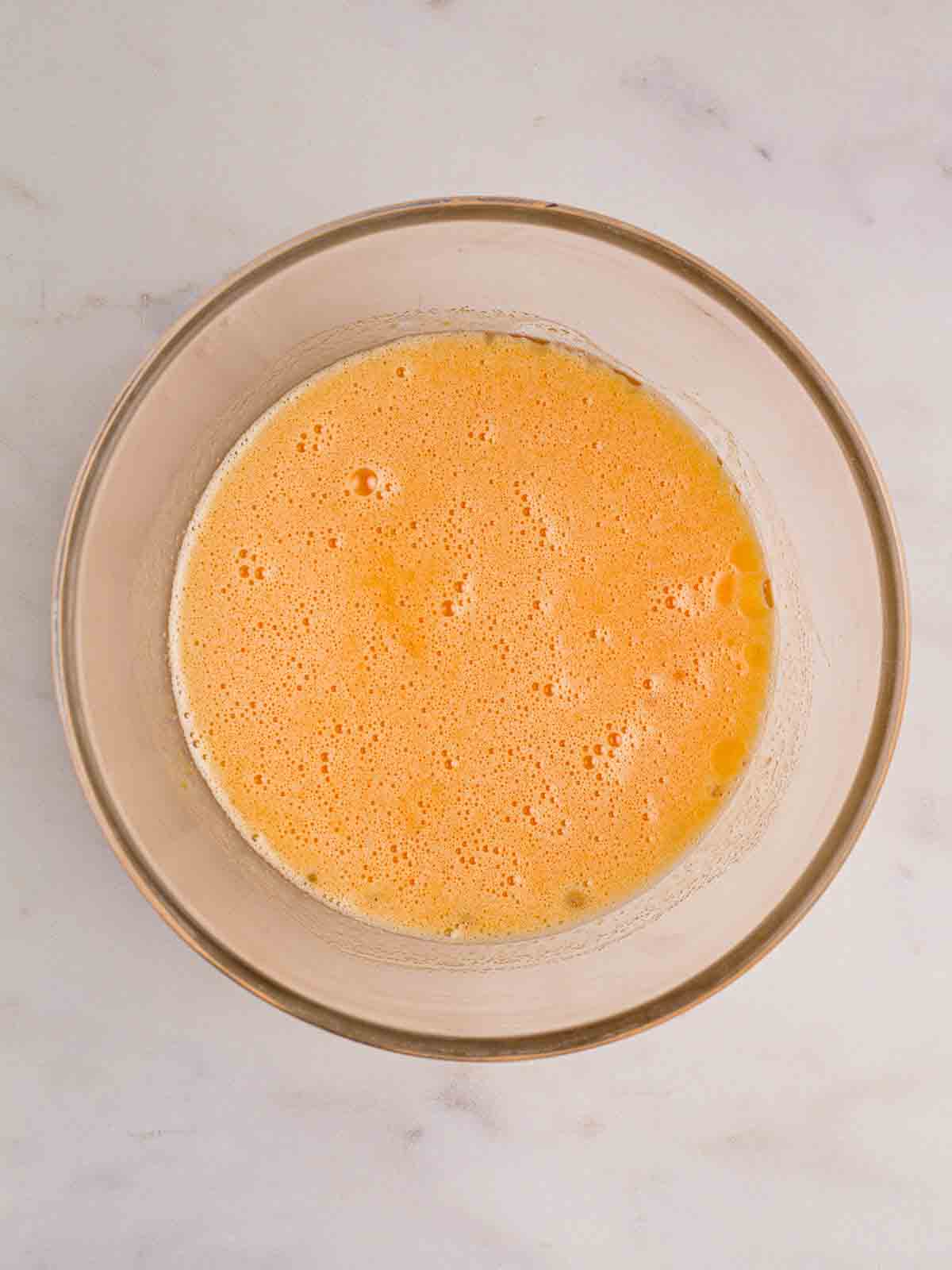 A bowl filled with mixed sugar, oil and eggs for step 2 in the recipe for Courgette Cake.