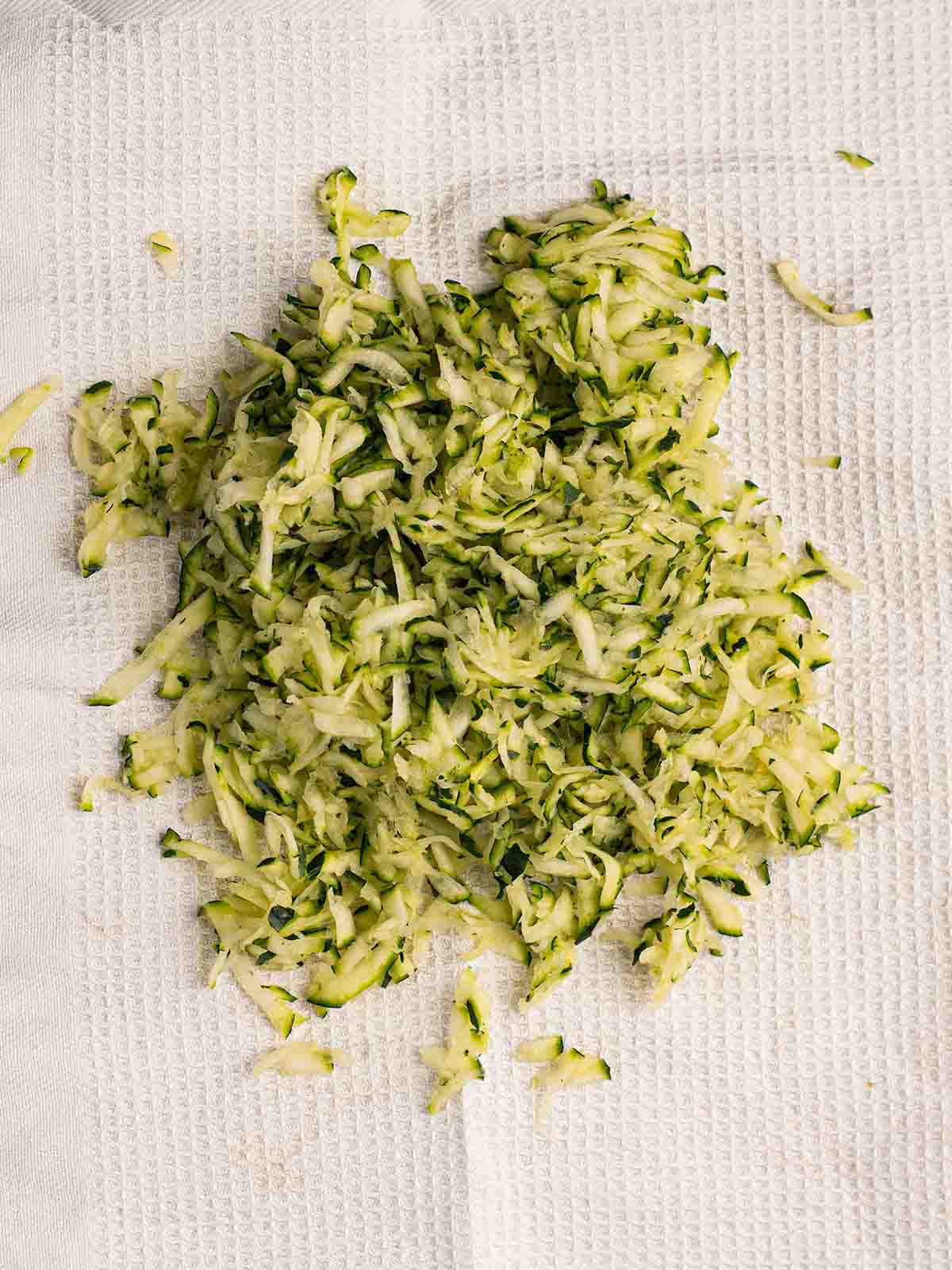 Grated courgettes on a tea towel, ready to be squeezed of water, for the first step in the recipe Courgette Cake.