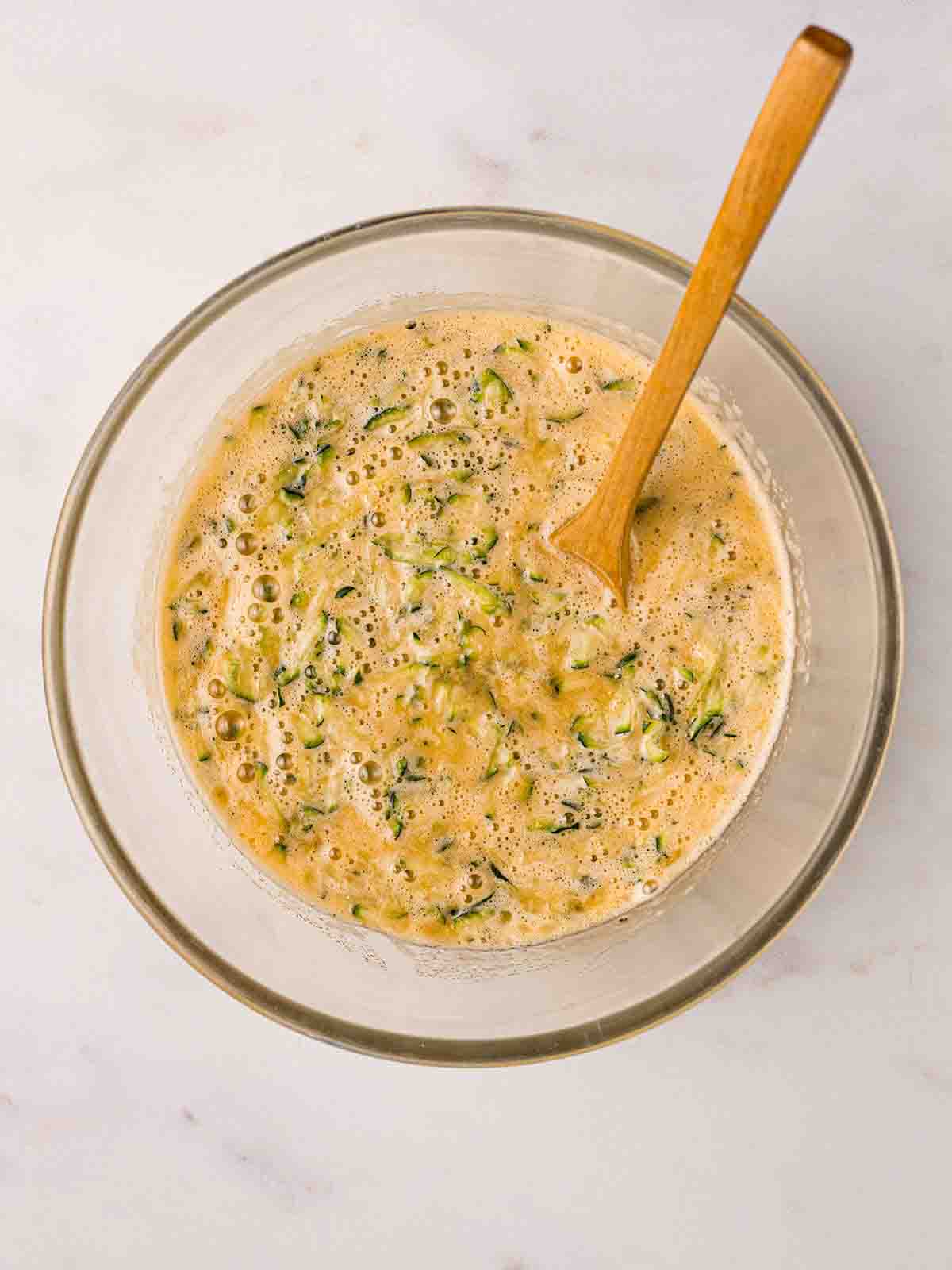 A glass bowl filled with eggs, sugar and oil as well as grated courgette for the recipe for Courgette Cake.