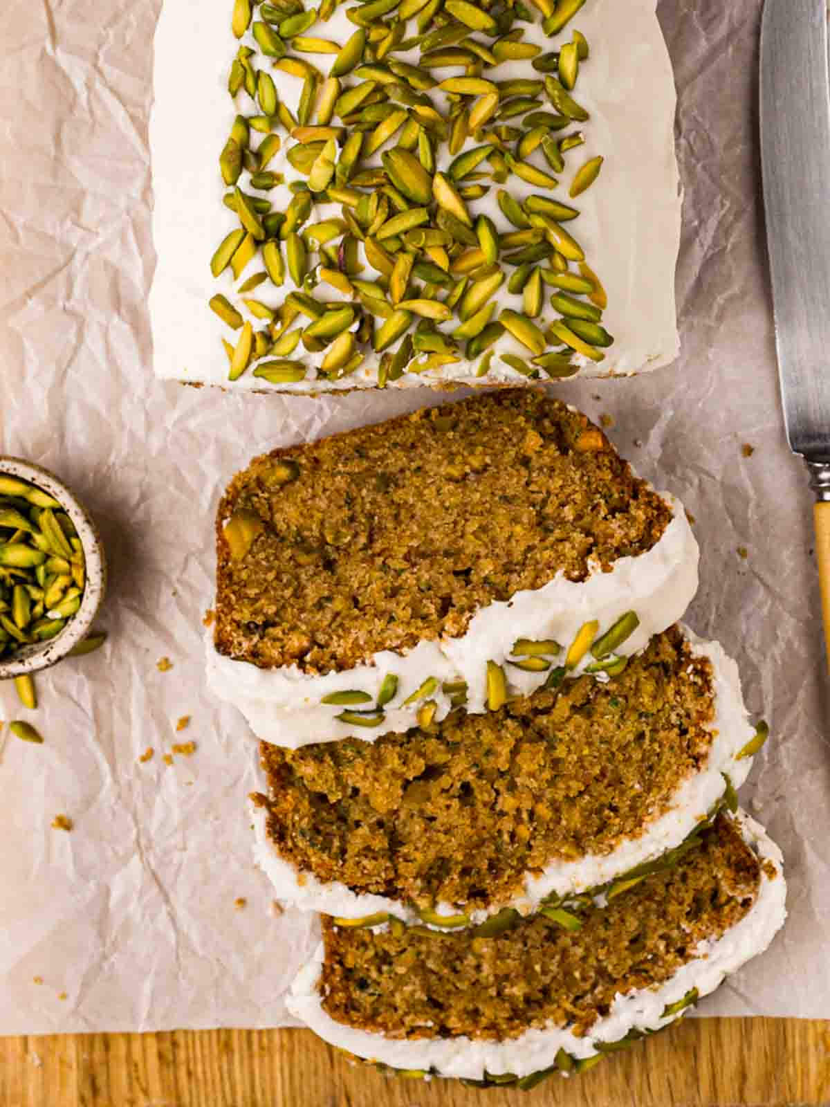A bird's eye view of a Courgette Cake, sliced with buttercream frosting and pistachios.