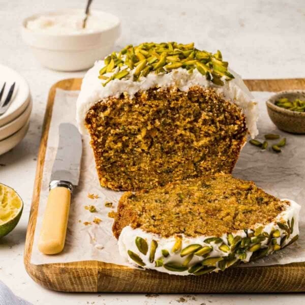 Inside of a courgette cake, sliced with knife on a board, surrounded by plates and bowls.