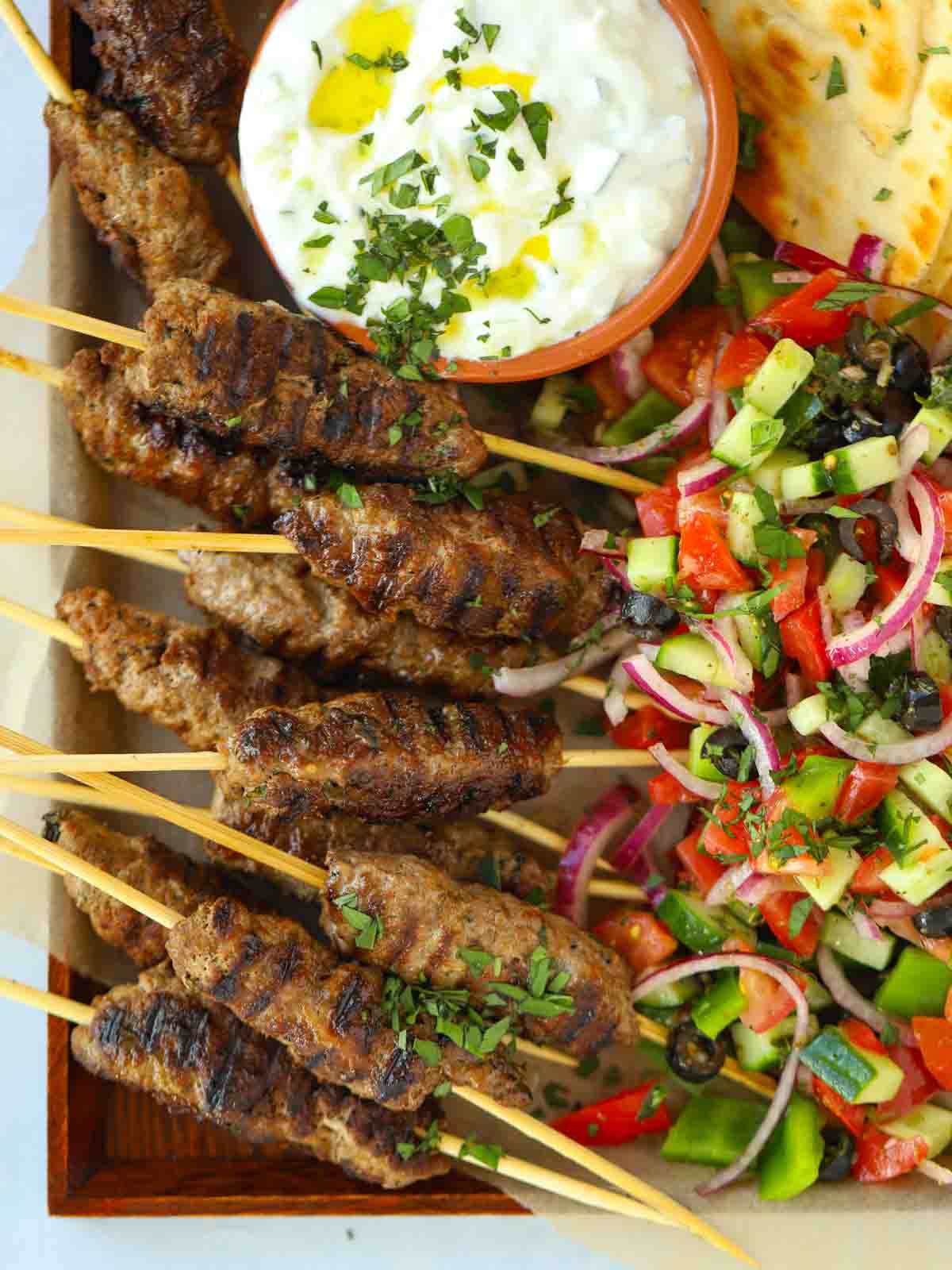 Lamb kofta kebabs recipe with flatbreads and Greek salad and tzatziki on a serving board, ready to eat.