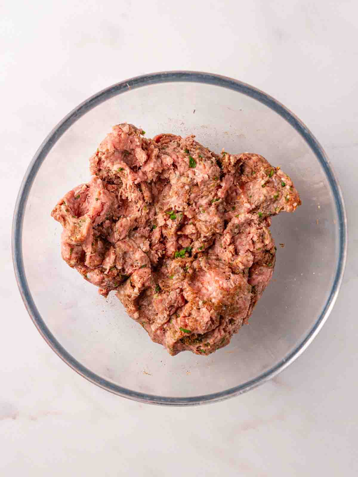 Raw lamb mince mixed with herbs in a glass bowl, ready to be turned into kebabs.
