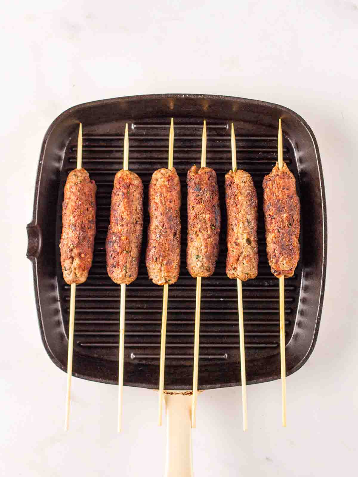 Lamb mince koftas with skewers cooking on a griddle pan for step 3 in the recipe method.