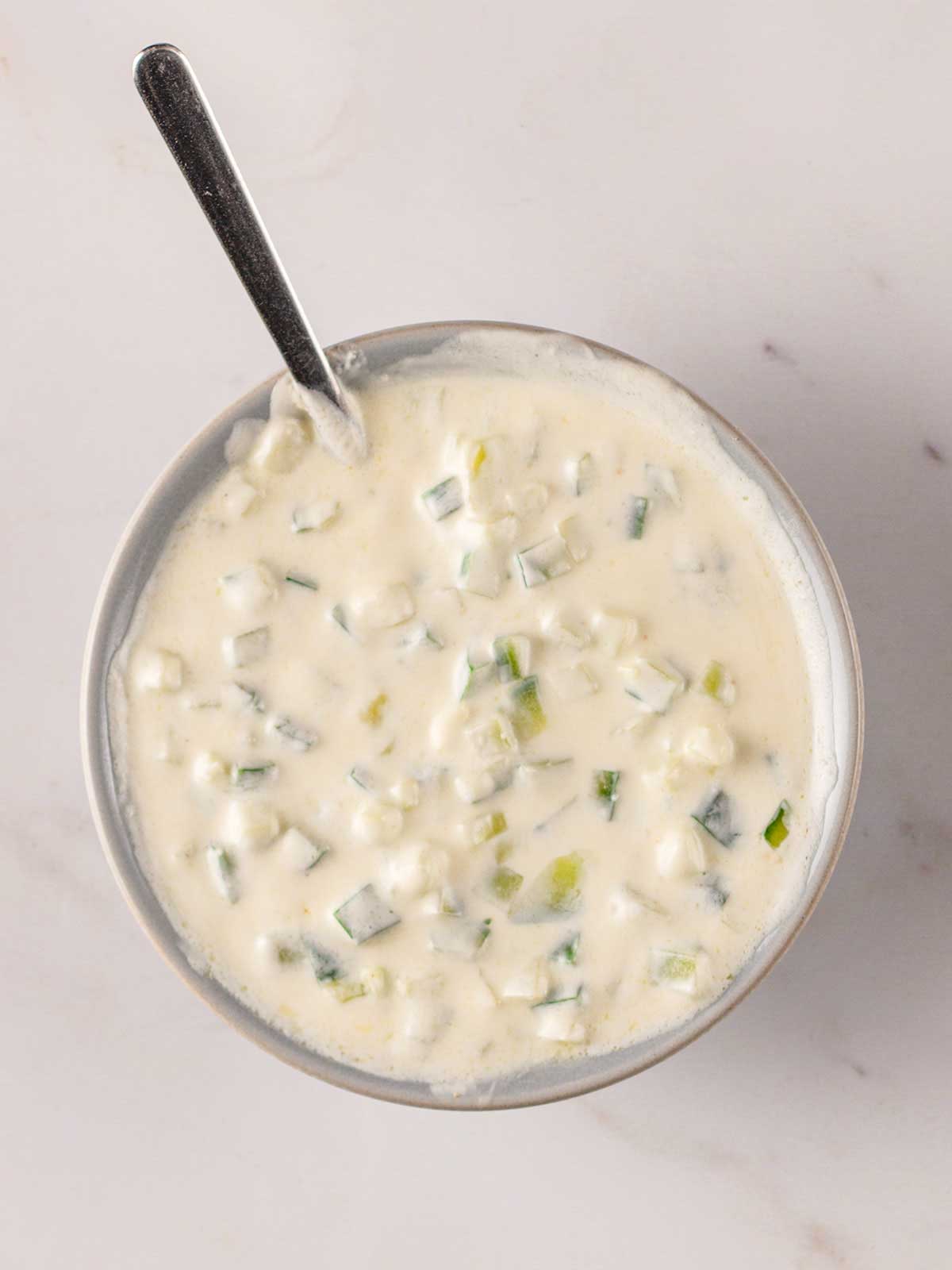 A bowl of homemade tzatziki with a spoon sticking out, ready to be served with lamb koftas.