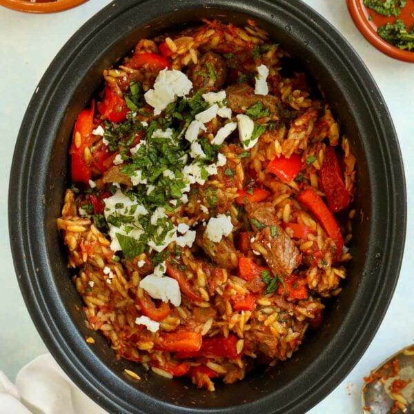 A slow cooker pan filled with Lamb Orzo Stew with feta cheese sprinkled over the top.