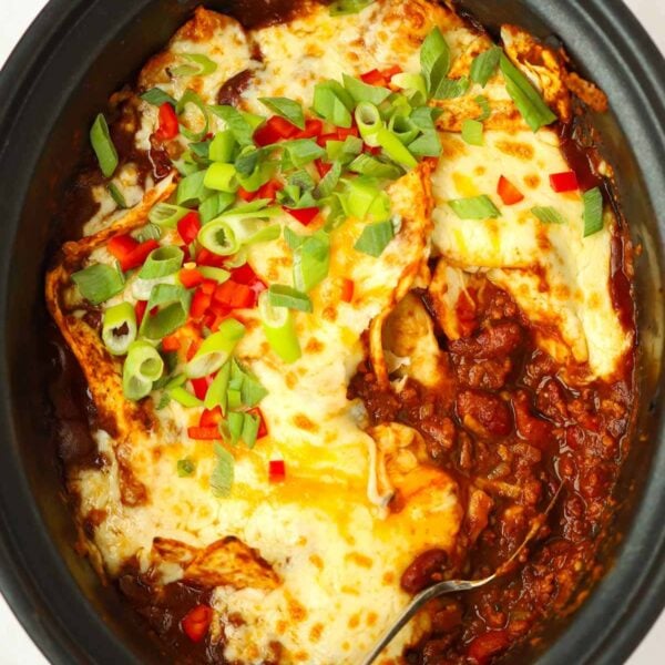 A slow cooker pan filled with cooked beef enchiladas with cheese on top.