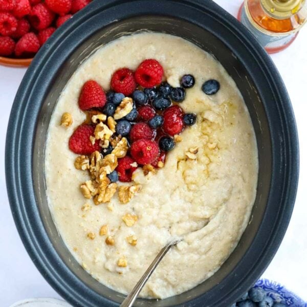A slow cooker pan filled with cooked Porridge, topped with berries and nuts.