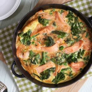A pan filled with cooked salmon frittata on a board on a table, with forks at the side.