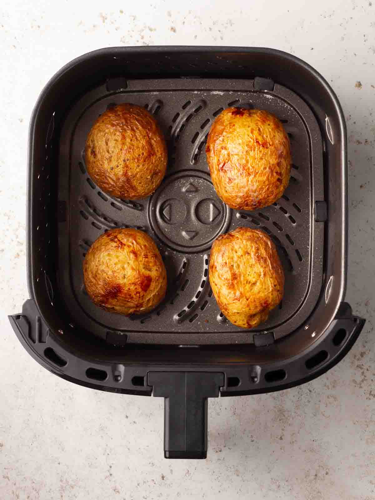 An air fryer with four cooked baked potatoes in side.