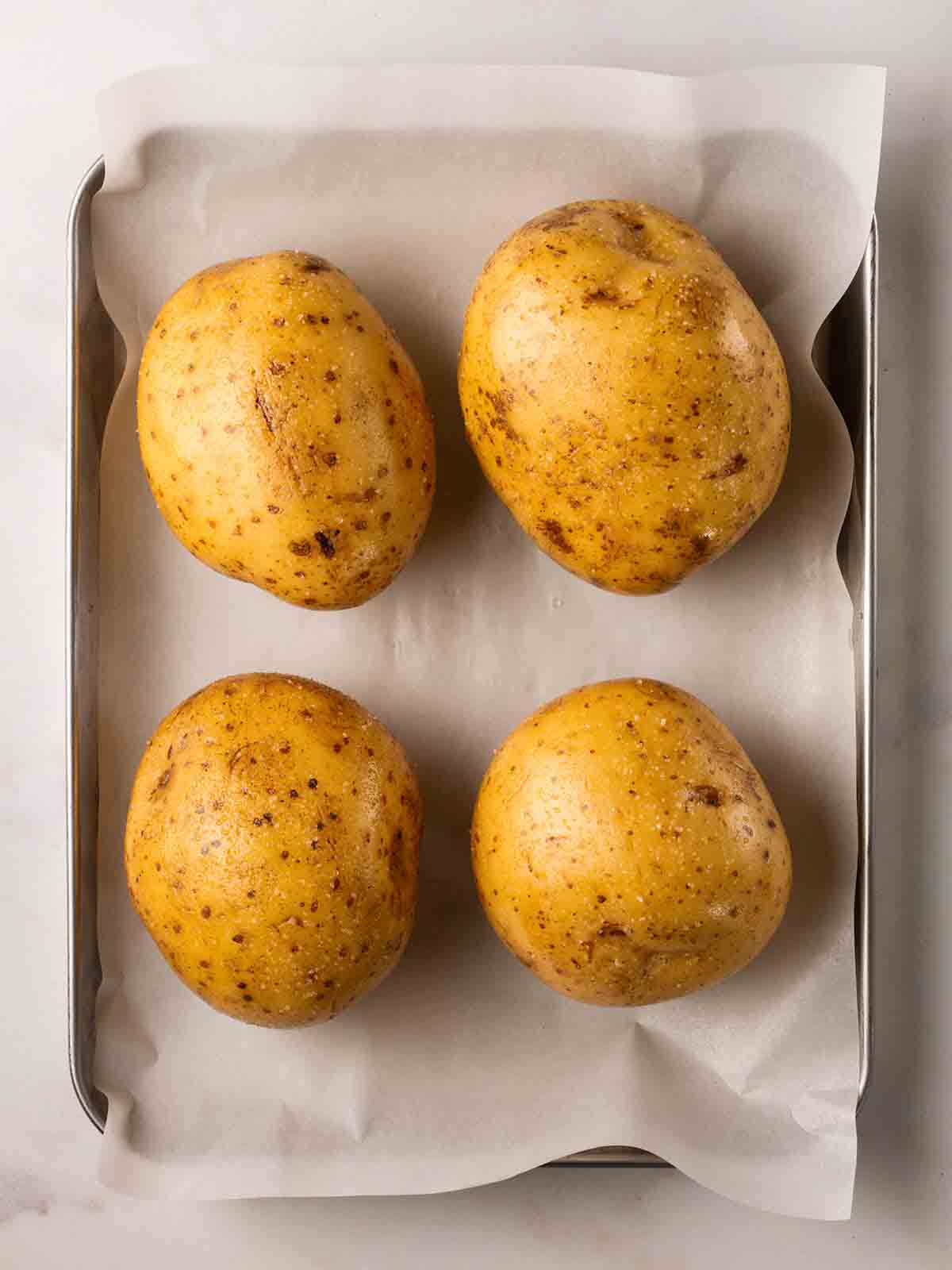 Four jacket potatoes on a baking tray, ready to be cooked in the air fryer.