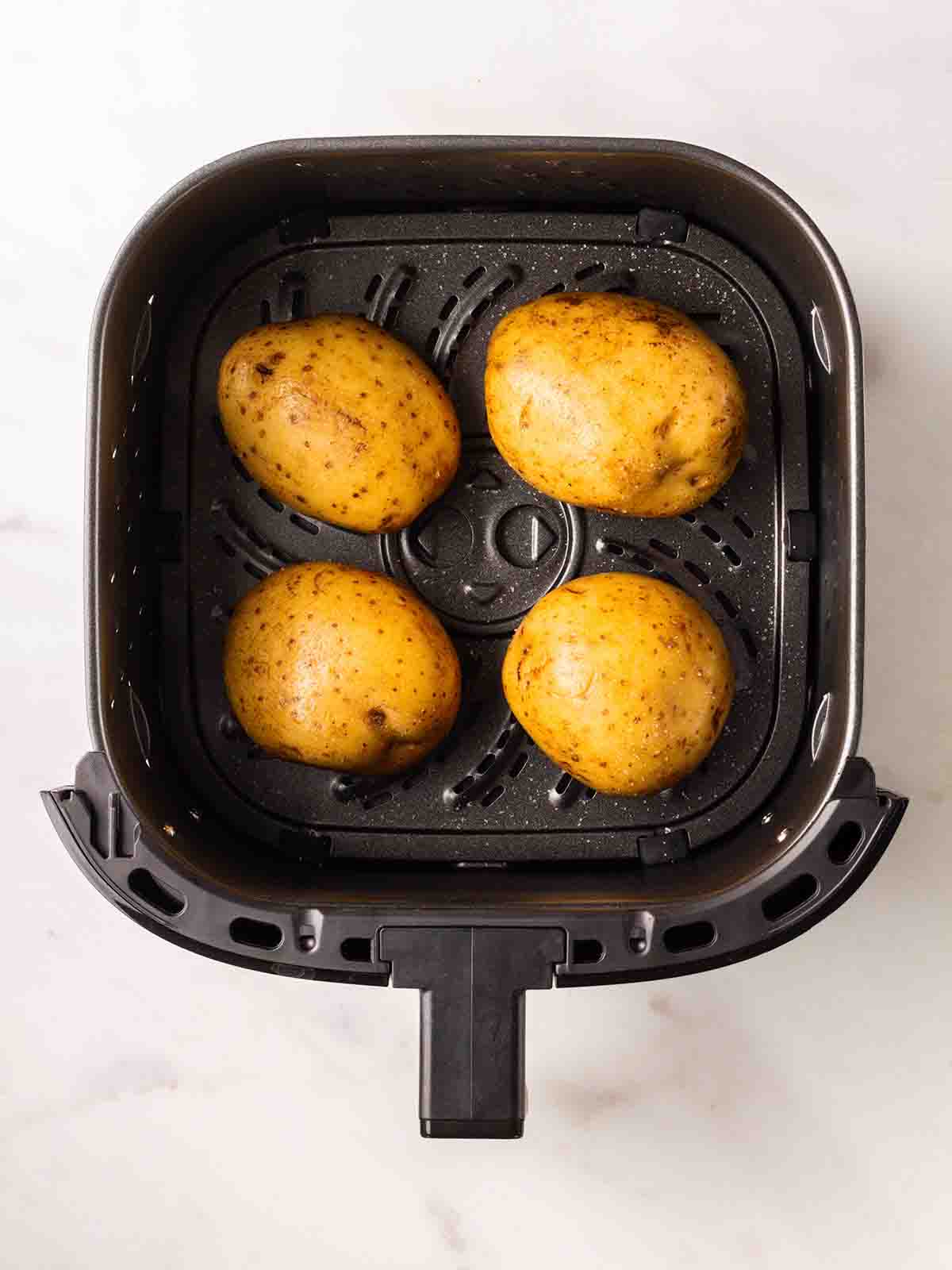 Four jacket potatoes in the air fryer, ready to be cooked.