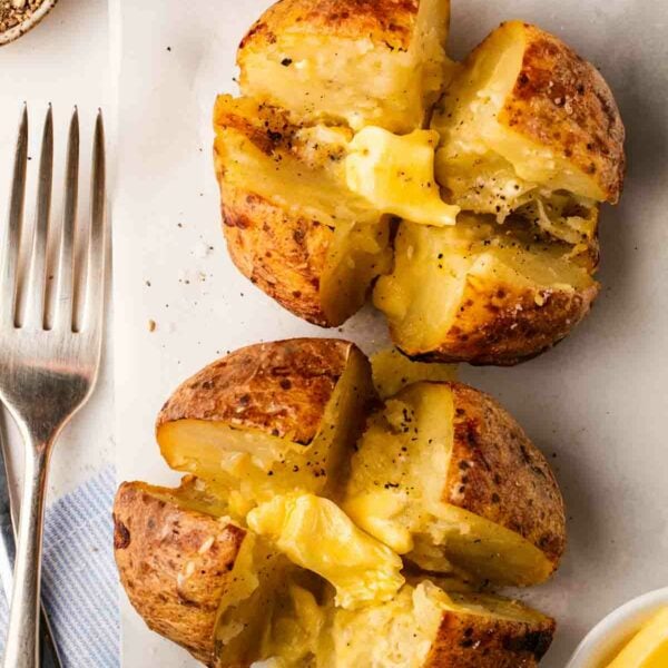 Two buttery cooked air fryer baked potatoes with a fork to the side, ready to eat.