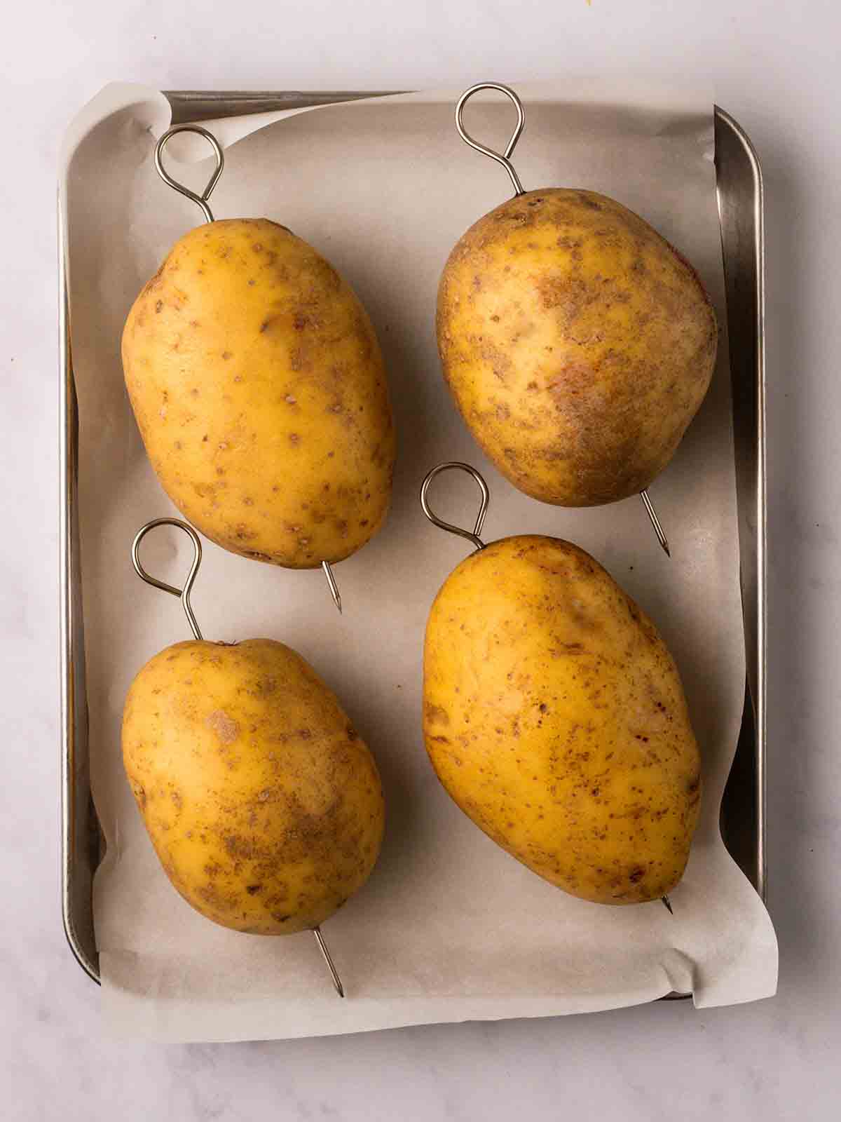 Four baked potatoes with skewers through the middle, ready to be cooked.