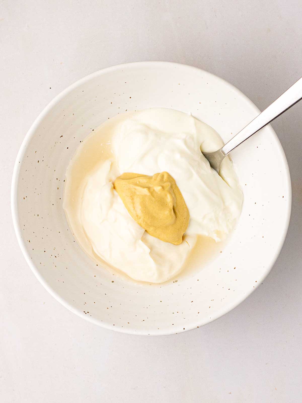 A white bowl with creamy dressing for step 1 in the process for making coleslaw.