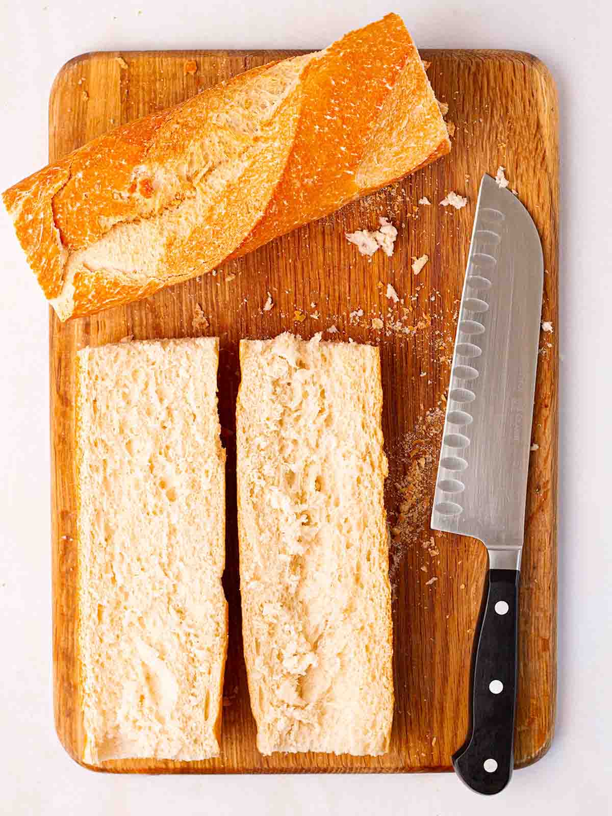 French bread cut in half on a chopping board for step 1 in the recipe for French Bread Pizza.